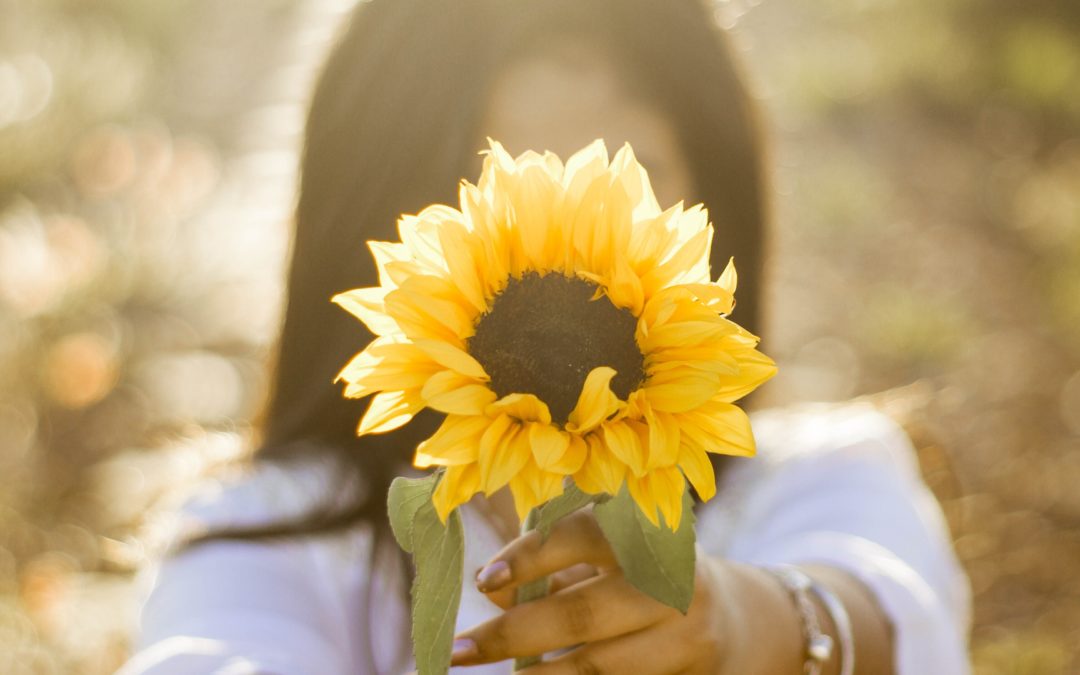 Frau hält Sonnenblume mit ausgestreckten Armen entgegen