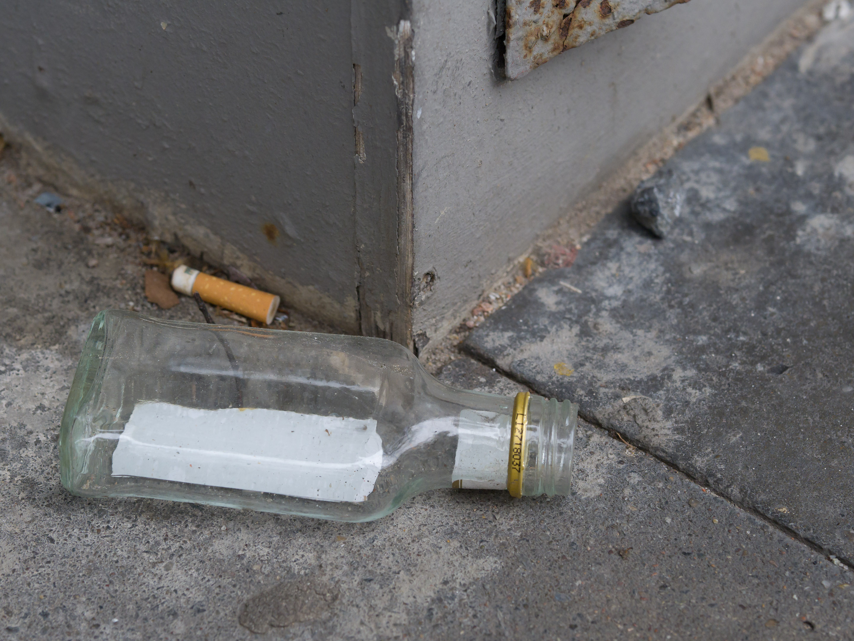 Schnapsflasche und Zigarettenkippe auf Betonplatten vor Gebäudeecke